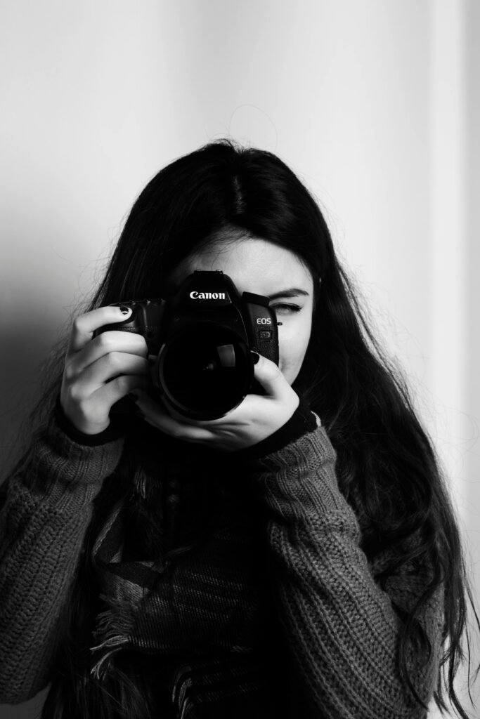 Portrait of a young woman taking a photo with a DSLR camera in a studio setting.